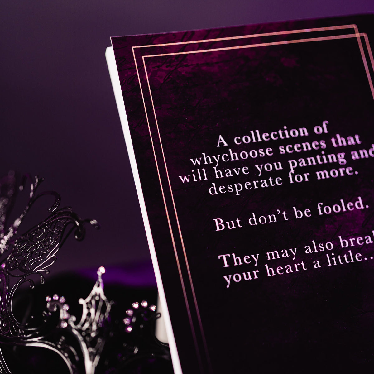 A dark gothic-themed book or card with white text on a black cover, styled with a silver masquerade mask and purple lighting against a dark background.